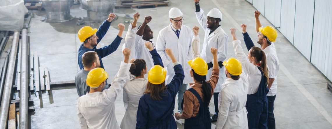 Group of factory workers and managers raising their fists together, illustrating union certification in a workplace.