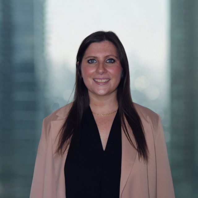 Alicia Ambrus, Associate Employment Lawyer at Achkar Law, professional headshot with city window backdrop.