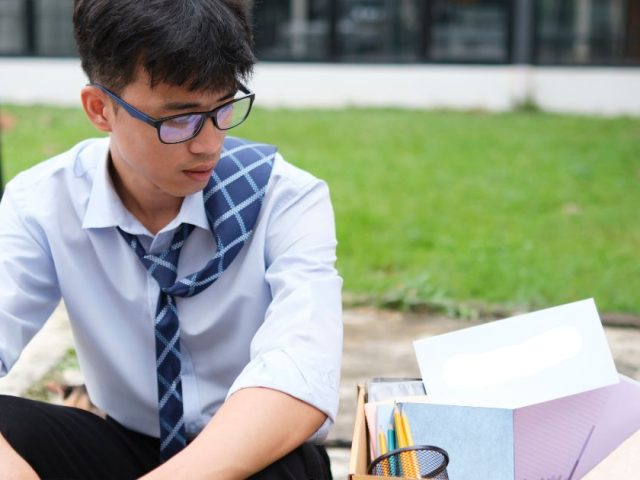 Young professional sitting outside with a box of belongings after dismissal, consequences of firing an employee in BC explained.
