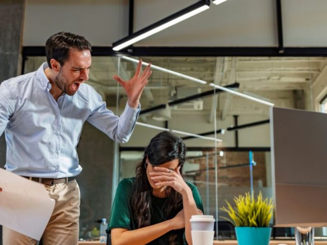 Angry manager yelling at distressed employee at her desk, retaliation in the workplace explained for British Columbia workers.