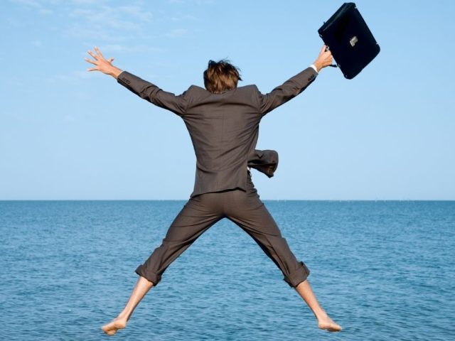 Businessman jumping joyfully over the ocean with briefcase in hand, vacation pay in BC and employee entitlements explained.