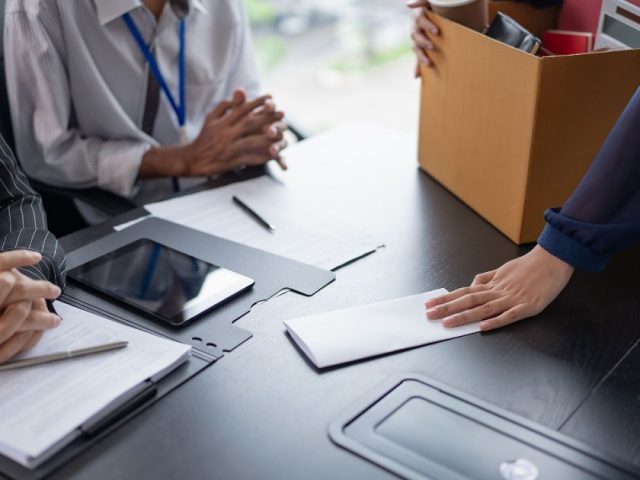 Employee handing in resignation letter with a box of belongings at a meeting, voluntary vs involuntary resignations in BC explained.