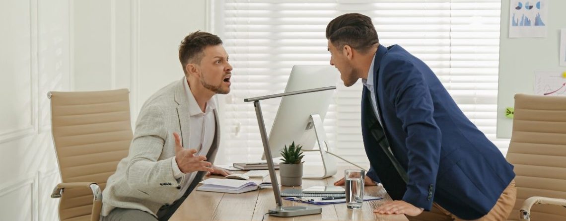 Two men in business attire arguing across an office desk, illustrating workplace misconduct in an Ontario workplace.