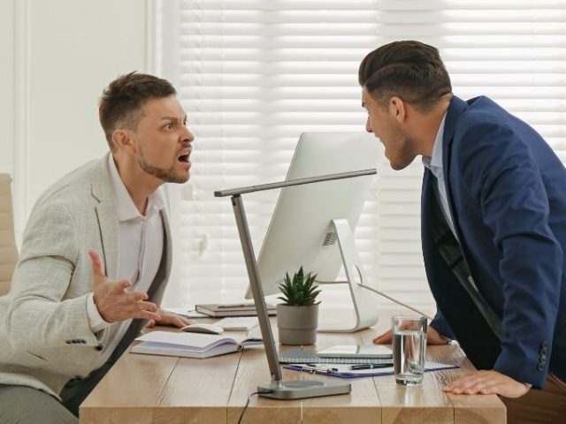 Two men in business attire arguing across an office desk, illustrating workplace misconduct in an Ontario workplace.