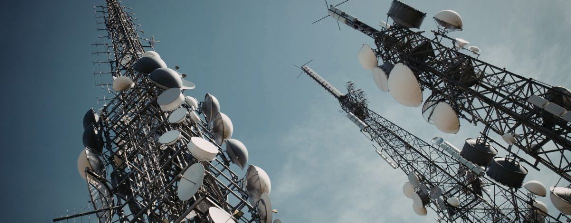 Telecommunications towers with satellite dishes against a blue sky, representing Bell Canada layoffs in the telecom sector.