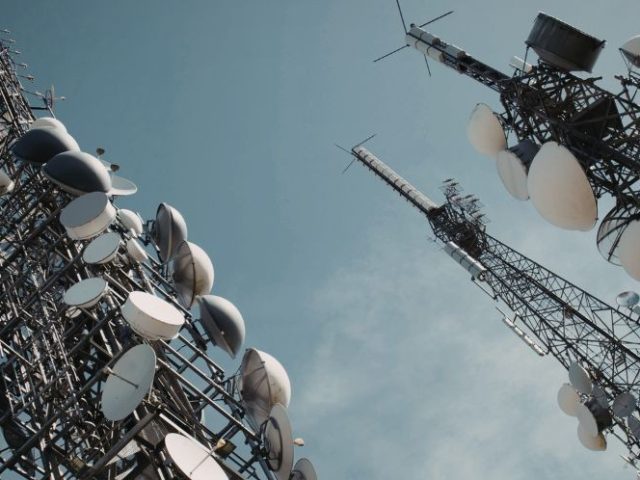 Telecommunications towers with satellite dishes against a blue sky, representing Bell Canada layoffs in the telecom sector.