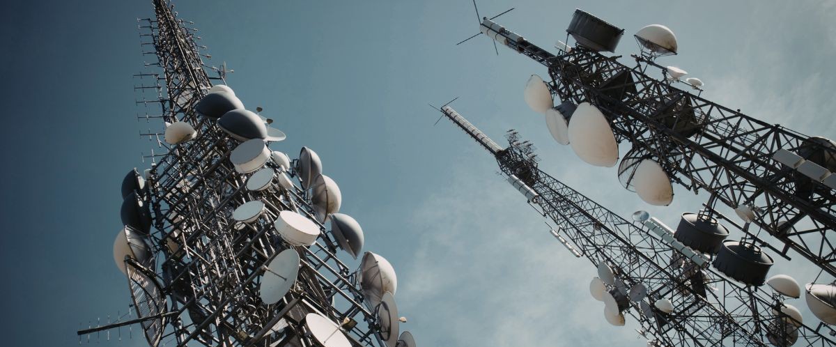 Telecommunications towers with satellite dishes against a blue sky, representing Bell Canada layoffs in the telecom sector.