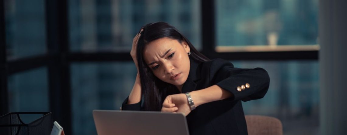 Tired employee checking watch at office desk late at night, understanding overtime pay in BC and employee entitlements.