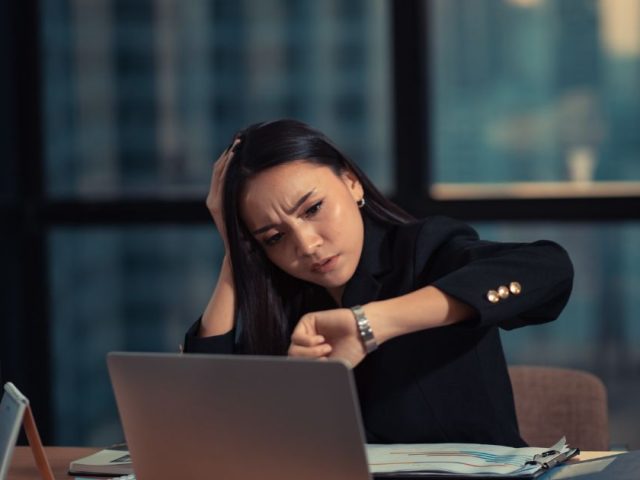 Tired employee checking watch at office desk late at night, understanding overtime pay in BC and employee entitlements.