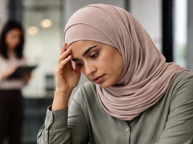 Woman in a hijab at her office desk looking concerned, illustrating workplace discrimination and HRTO complaints.