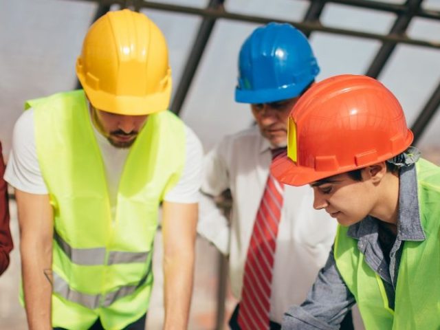 Construction workers in hard hats and safety vests reviewing plans on a building site, representing the BC construction context of the Parolin v. Cressey case.