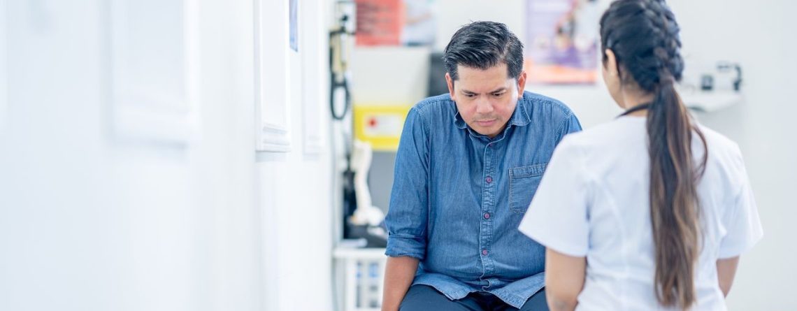 Man seated in a clinic looking down while speaking with a healthcare provider, illustrating mental health leave in Ontario.