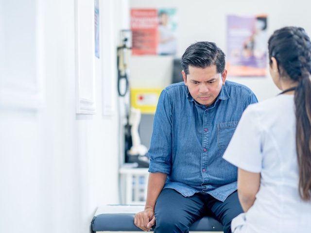 Man seated in a clinic looking down while speaking with a healthcare provider, illustrating mental health leave in Ontario.