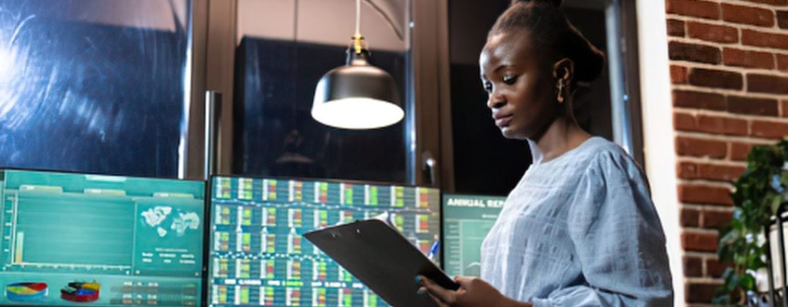 A woman reviewing multiple monitors displaying employee activity data and analytics dashboards.