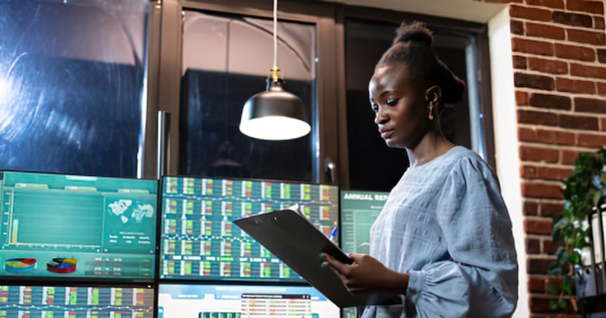 A woman reviewing multiple monitors displaying employee activity data and analytics dashboards.